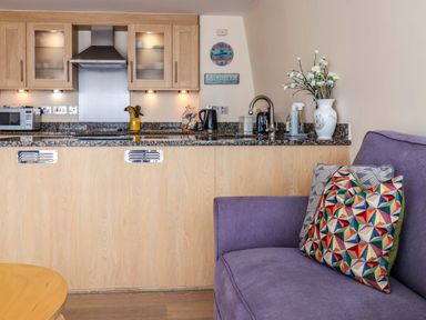 A kitchen with wooden cabinets and granite countertop next to a purple sofa with colorful patterned cushions at 2 Driftwood in West Bay