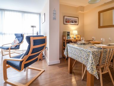 A dining area with a table covered in a floral tablecloth and set for four next to a living area with two blue cushioned wooden chairs at 2 Driftwood in West Bay