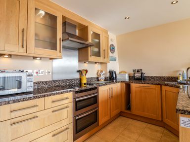 A kitchen with wooden cabinets a microwave oven kettle toaster and sink at 2 Driftwood in West Bay