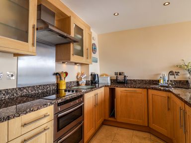 A kitchen with wooden cabinets granite countertops a stovetop oven sink and small appliances at 2 Driftwood in West Bay