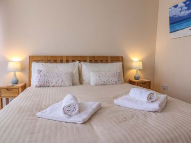 A bedroom with a wooden bed frame and bedside tables with lamps at 2 Driftwood in West Bay
