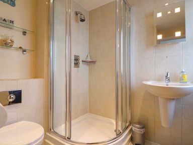 A bathroom with a corner shower enclosure a sink a mirror a toilet and glass shelves at 2 Driftwood in West Bay