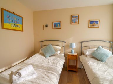 A bedroom with two single beds a nightstand with a lamp between them and framed pictures on the wall at 2 Driftwood in West Bay