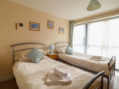 A bedroom with two single beds a bedside table with a lamp and framed pictures on the wall at 2 Driftwood in West Bay