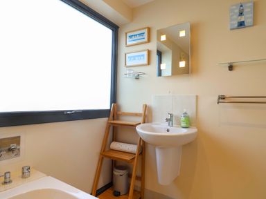 A bathroom with a bathtub a sink with soap a wooden shelf a mirror and framed pictures at 2 Driftwood in West Bay