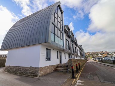 A modern building with curved metal roof and windows along a street at 2 Driftwood in West Bay