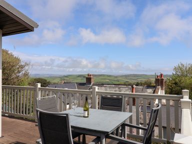 A balcony with a table and four chairs overlooking rooftops and green hills at High Bullen Lodge in Morcombelake