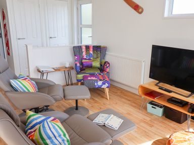 A living room with a television on a wooden stand two armchairs with striped pillows a patterned chair a small wooden side table and wooden flooring at High Bullen Lodge in Morcombelake