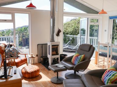 A living room with leather chairs and a fireplace next to a dining table with white chairs at High Bullen Lodge in Morcombelake