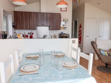 A dining table set with plates and glasses next to a kitchen with brown cabinets and appliances at High Bullen Lodge in Morcombelake