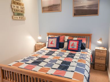 A bedroom with a wooden double bed colorful checkered bedding two bedside tables with lamps and wall art above the bed at High Bullen Lodge in Morcombelake