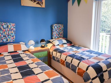 A bedroom with two single beds with patterned bedding and a blue accent wall at High Bullen Lodge in Morcombelake
