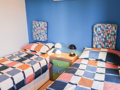 A bedroom with two single beds with colorful checkered bedding and a nightstand with two lamps against a blue wall at High Bullen Lodge in Morcombelake