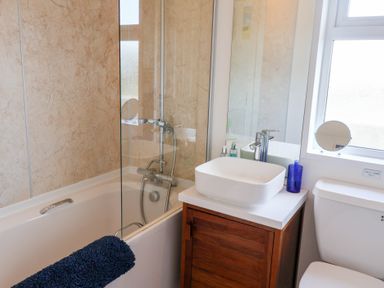 A bathroom with a bathtub shower combination a wooden vanity with a white vessel sink a toilet and a window at High Bullen Lodge in Morcombelake