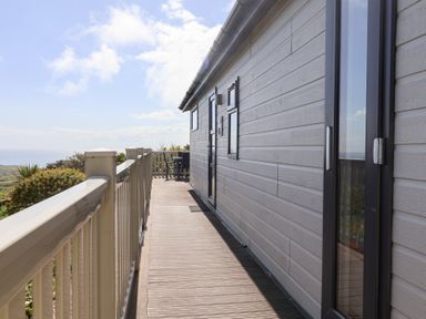 A wooden deck with railings along a building exterior and outdoor furniture at High Bullen Lodge in Morcombelake