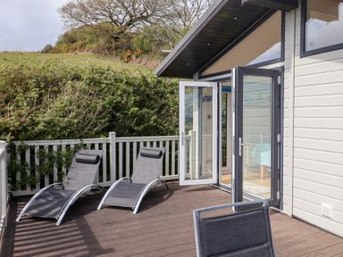 An outdoor deck with two lounge chairs and open glass doors leading inside at High Bullen Lodge in Morcombelake
