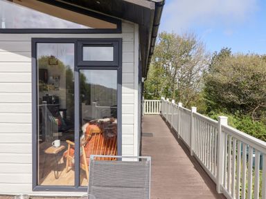 A balcony with a white railing next to a building with large glass windows and a chair inside at High Bullen Lodge in Morcombelake