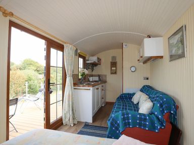 A small living area with a kitchenette and a couch covered with a blue patterned throw at Llety'r Bugail 1 in Llanrug