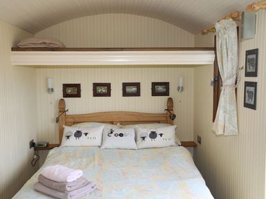 A bedroom with a bed with sheep pillows blankets folded on the bed and framed pictures on the wall at Llety'r Bugail 1 in Llanrug