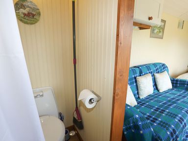 A small bathroom with a white toilet and broom next to a living area with a blue patterned sofa and pillows at Llety'r Bugail 1 in Llanrug