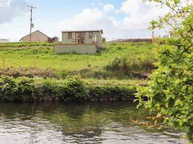 A small green building on a grassy hill overlooking a body of water at Llety'r Bugail 1 in Llanrug