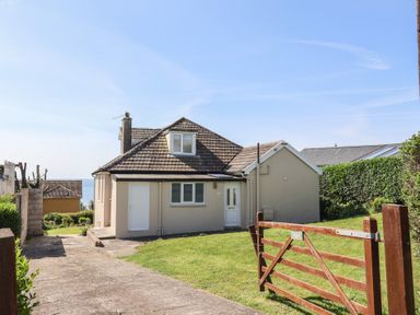 A house with a tiled roof a driveway and a wooden gate with grass lawn at Tillicum in Charmouth