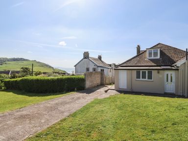 A house with a driveway and lawn with green hedges and sea view at Tillicum in Charmouth