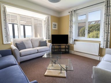 A living room with sofas a glass coffee table a television and windows at Tillicum in Charmouth