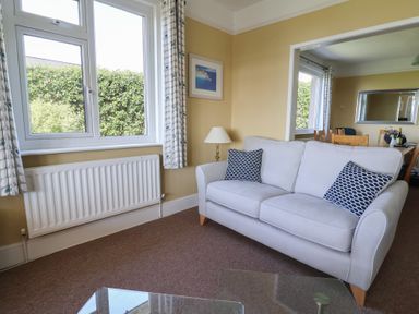 A living room with a sofa and cushions next to a window with curtains and a lamp at Tillicum in Charmouth