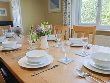 A dining table set with white plates bowls wine glasses and cutlery with a vase of flowers at Tillicum in Charmouth