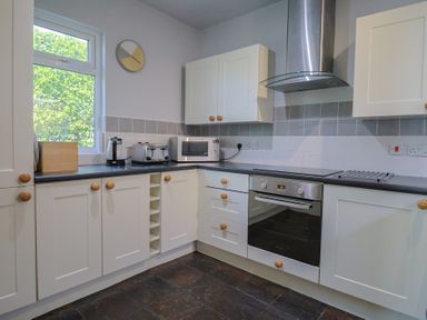 A kitchen with white cabinets a built in oven a microwave toaster and a window at Tillicum in Charmouth