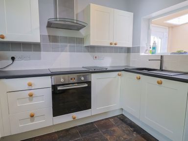 A kitchen with white cabinets wooden knobs an oven cooktop and a sink under a window at Tillicum in Charmouth