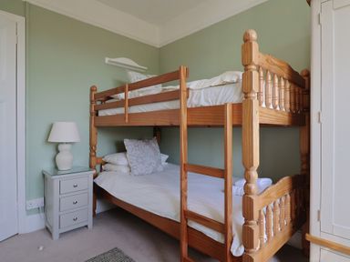 A bedroom with a wooden bunk bed a bedside table with a lamp and a wardrobe at Tillicum in Charmouth