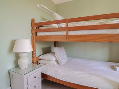A bedroom with wooden bunk beds and a bedside table with a lamp at Tillicum in Charmouth
