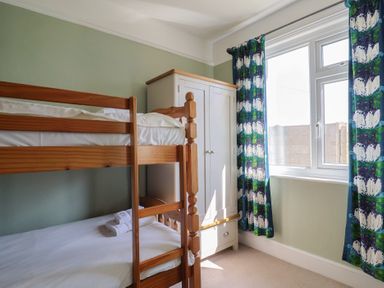 A bedroom with wooden bunk beds a white wardrobe and a window with patterned blue curtains at Tillicum in Charmouth