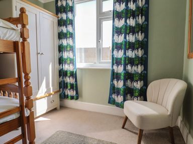 A bedroom corner with a wooden bunk bed a white wardrobe colorful curtains and a cream chair at Tillicum in Charmouth