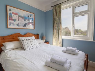 A bedroom with a wooden bed frame white bedding and two stacks of towels on the bed at Tillicum in Charmouth