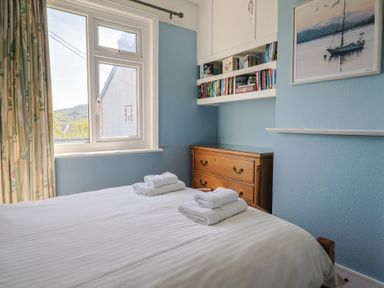 A bedroom with a bed and folded towels next to a window and a wooden dresser with shelves above at Tillicum in Charmouth