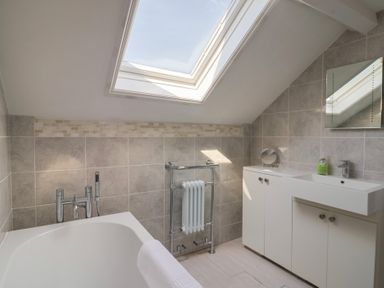 A bathroom with a bathtub, sink with cabinets, towel radiator, and skylight window at Tillicum in Charmouth
