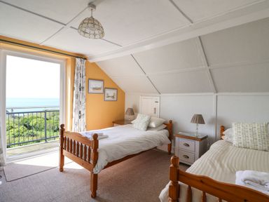 A bedroom with two single wooden beds and a balcony overlooking greenery and the ocean at Tillicum in Charmouth