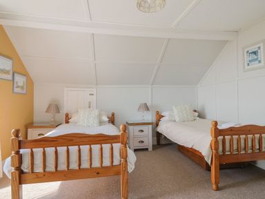 A bedroom with two wooden single beds two nightstands and lamps at Tillicum in Charmouth