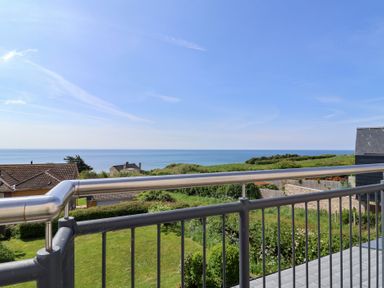 A balcony with metal railings overlooking green gardens houses and the sea at Tillicum in Charmouth