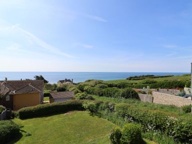 A view of the sea with houses and grassy gardens in the foreground at Tillicum in Charmouth