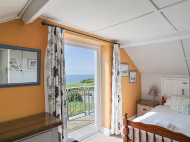 A bedroom with a wooden bed beside a nightstand and a sliding door leading to a balcony with an ocean view at Tillicum in Charmouth