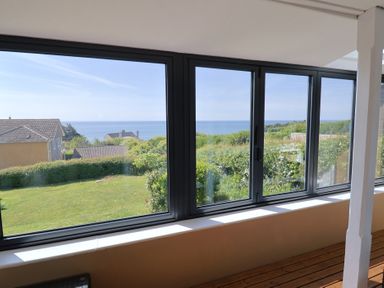 A large window with a view of houses a garden and the sea at Tillicum in Charmouth
