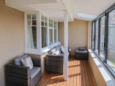 A sunroom with rattan armchairs and a cushioned bench along windows at Tillicum in Charmouth