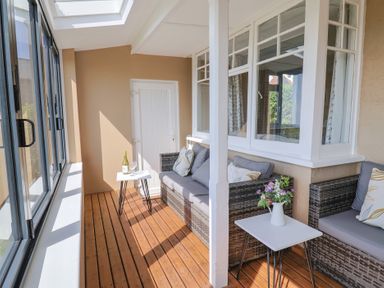 A sunroom with wicker sofas and side tables with a bottle and glasses at Tillicum in Charmouth
