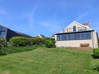 A house with a balcony and large windows overlooking a grassy yard with bushes at Tillicum in Charmouth