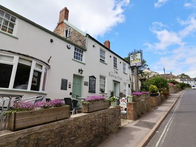 The exterior of a building with flower boxes along a stone wall a sign reading Royal Oak and outdoor seating at Tillicum Charmouth