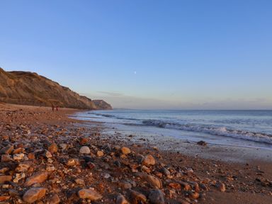 A pebble beach with waves and cliffs in the background at Tillicum in Charmouth